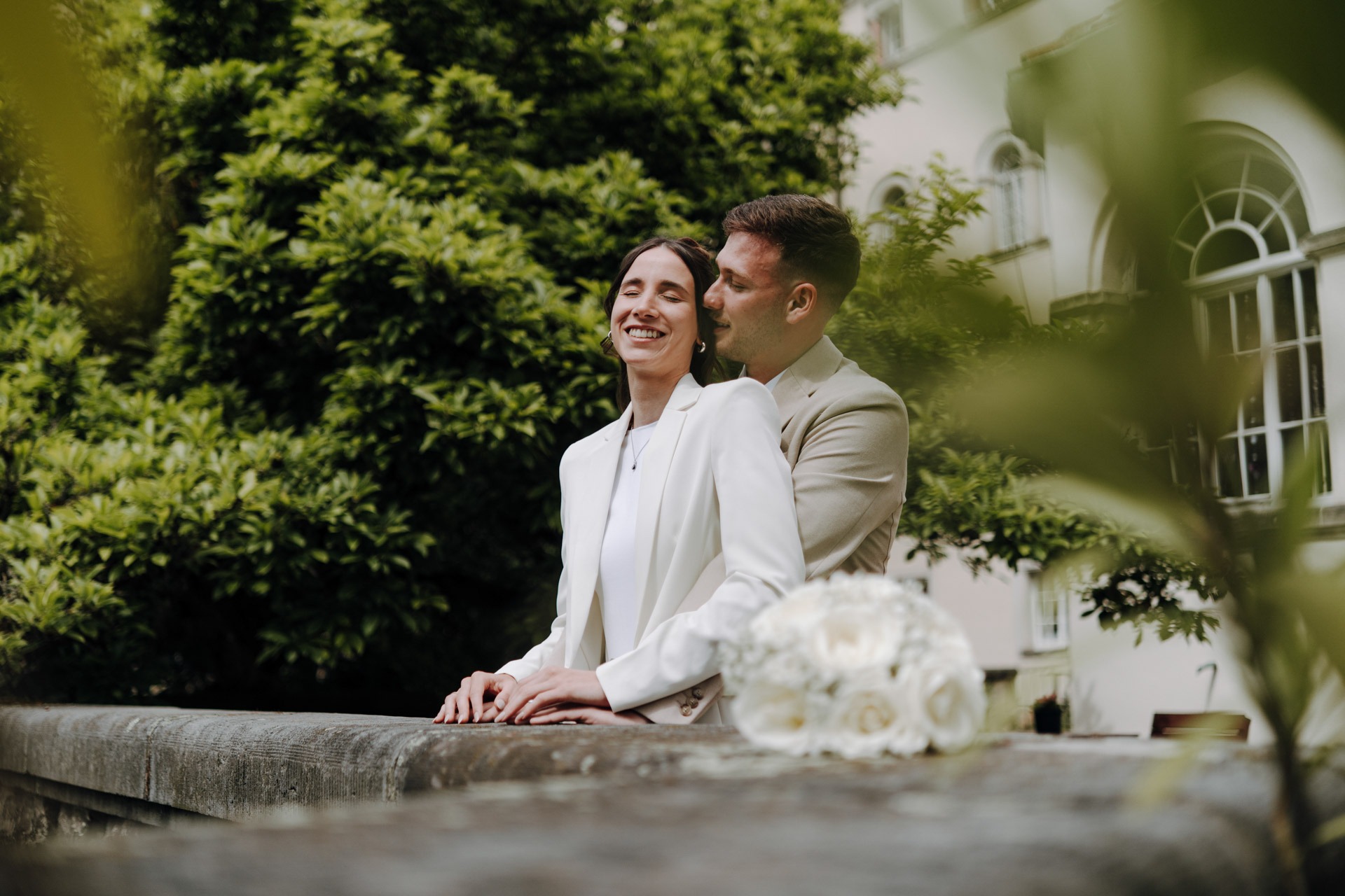 Melissa und Lukas sitzen gemeinsam an einer hellen Steinbrüstung im Park.