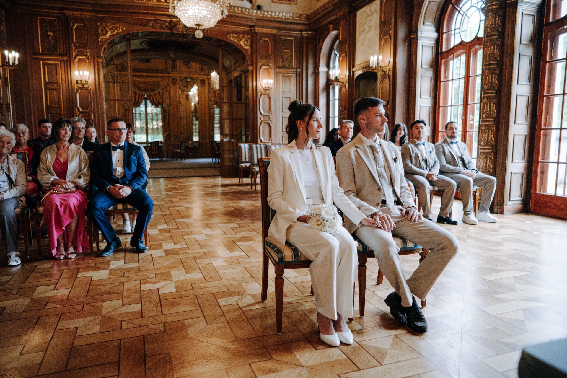 Melissa und Lukas sitzen während ihrer standesamtlichen Trauung mit ihren Gästen im historischen Trauzimmer.