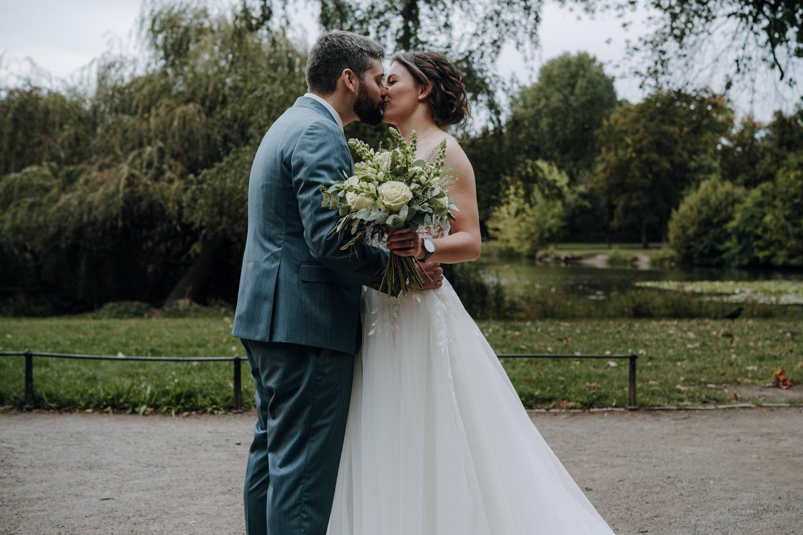 Luisa und Jonas stehen einander auf einem Parkweg gegenüber, Blätter rahmen das Bild ein.