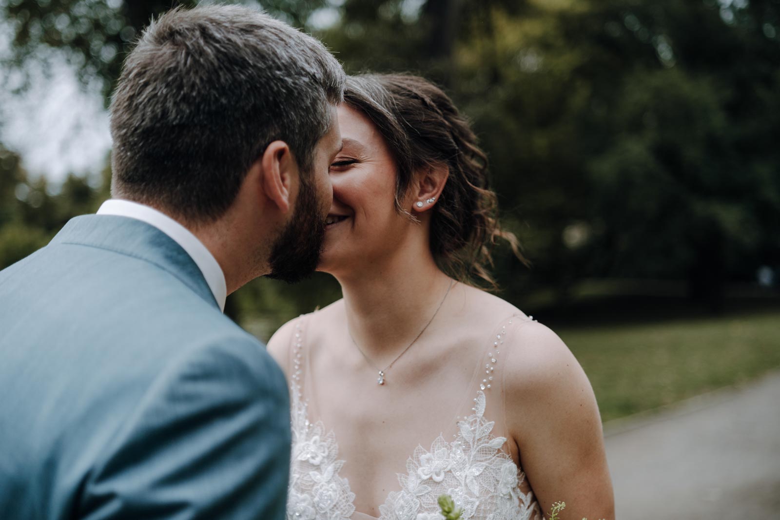 Luisa und Jonas küssen sich im Park, Luisa hält einen hellen Brautstrauß zwischen ihnen.