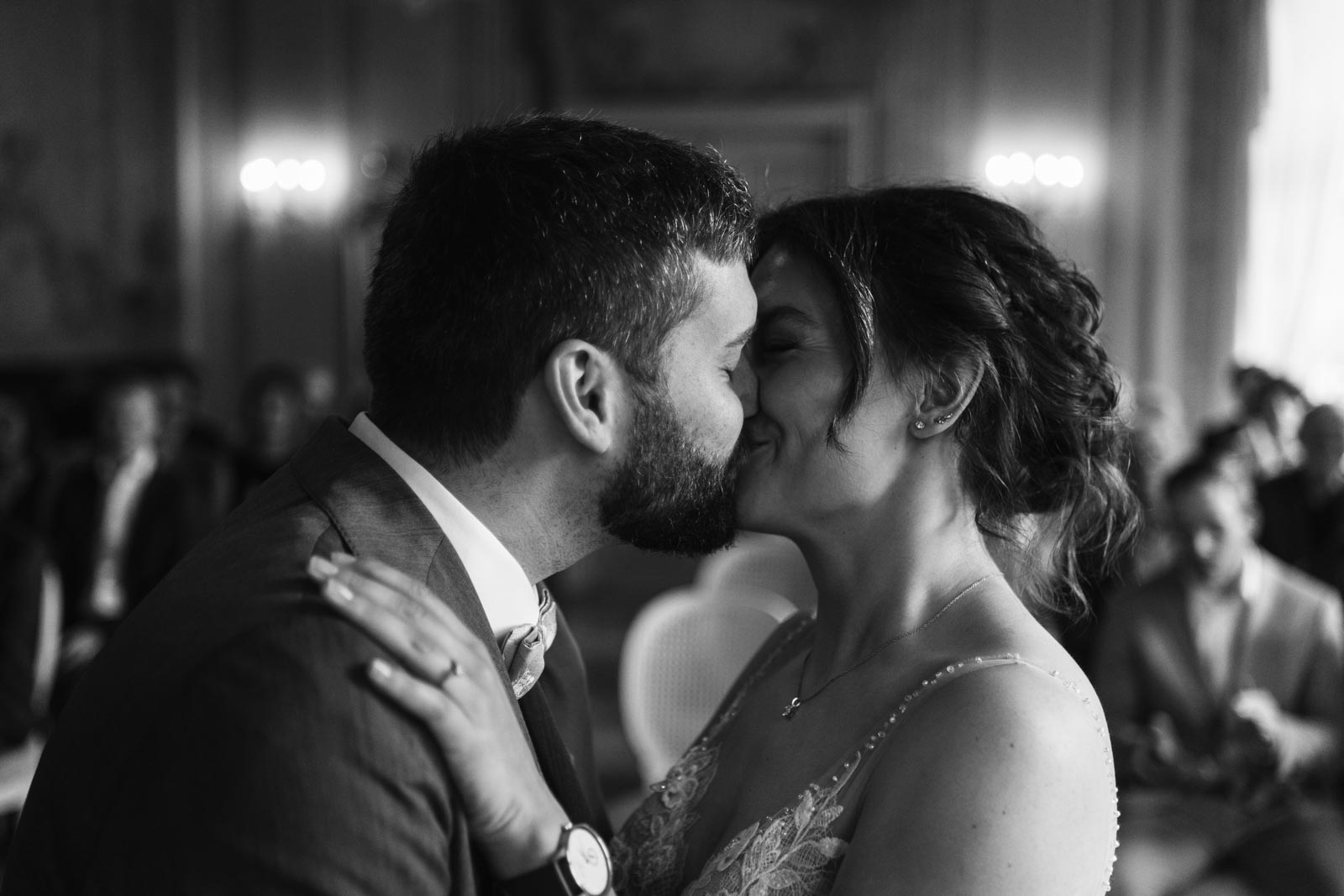Luisa und Jonas küssen sich im Trausaal, ihre Gäste sind im Hintergrund zu sehen.
