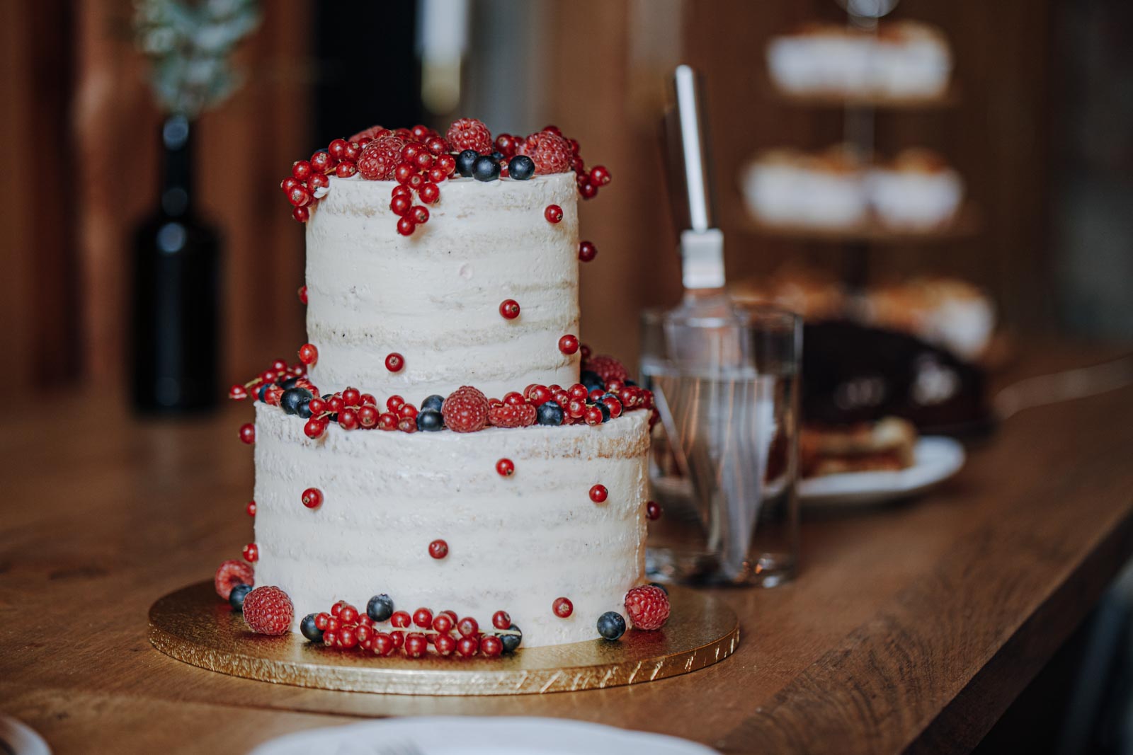 Eine zweistöckige helle Hochzeitstorte mit roten Beeren steht auf einem Holztisch.
