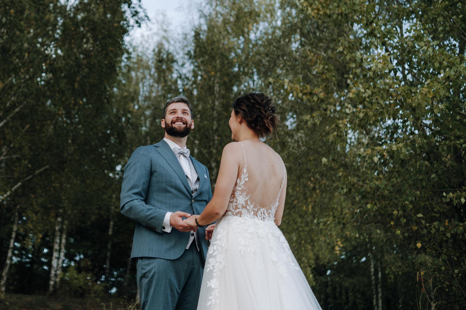 Jonas lacht, während er Luisa an den Händen hält; Bäume bilden den Hintergrund.